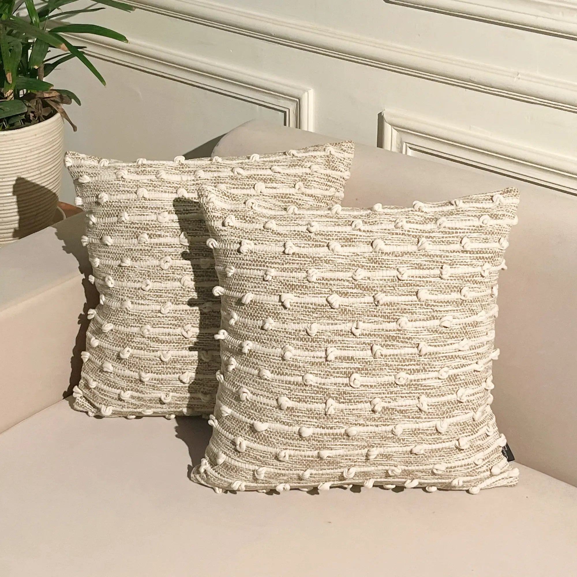 Two textured cotton cushions on a bench beside a potted plant