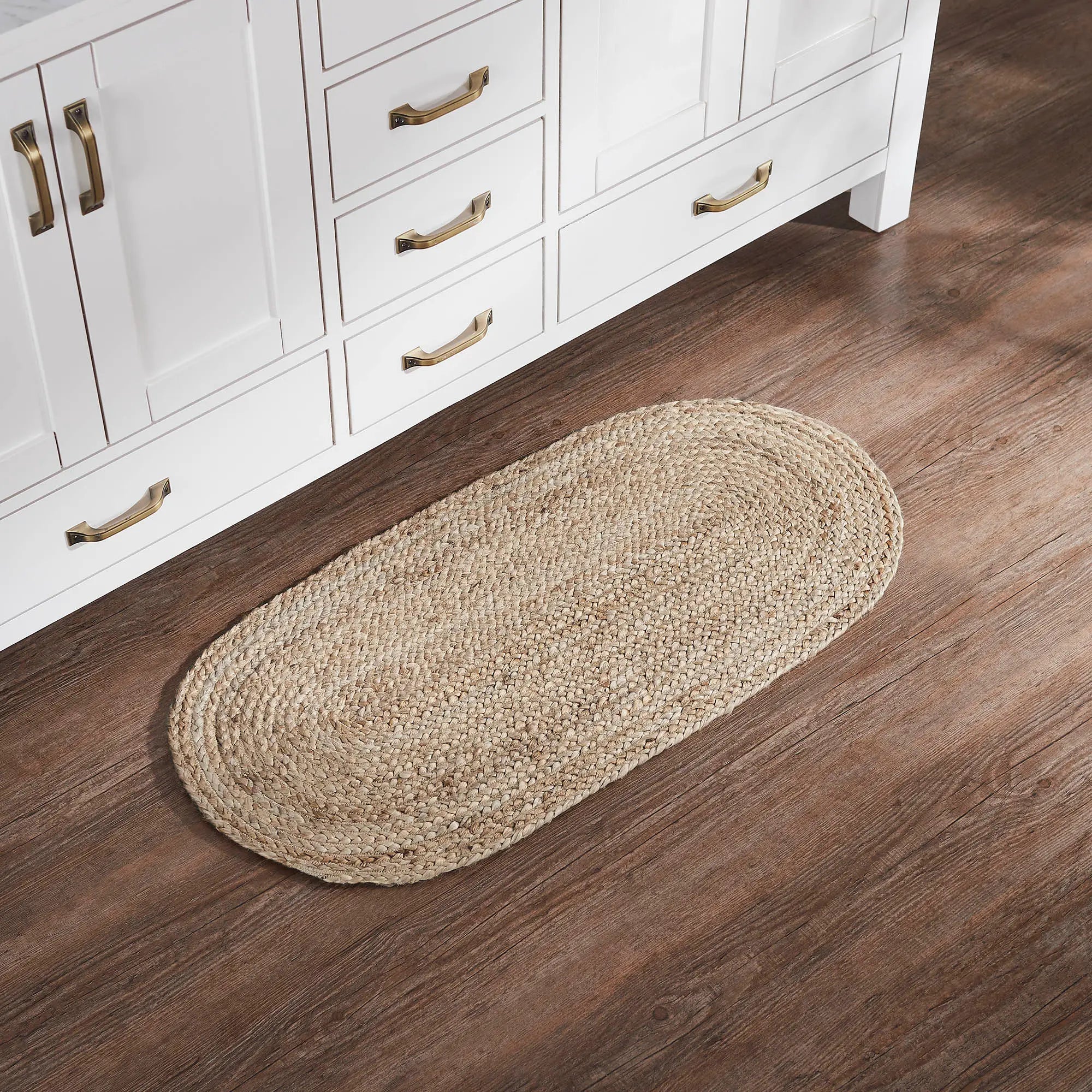 An oval braided jute rug on a wooden floor beside a painted cabinet